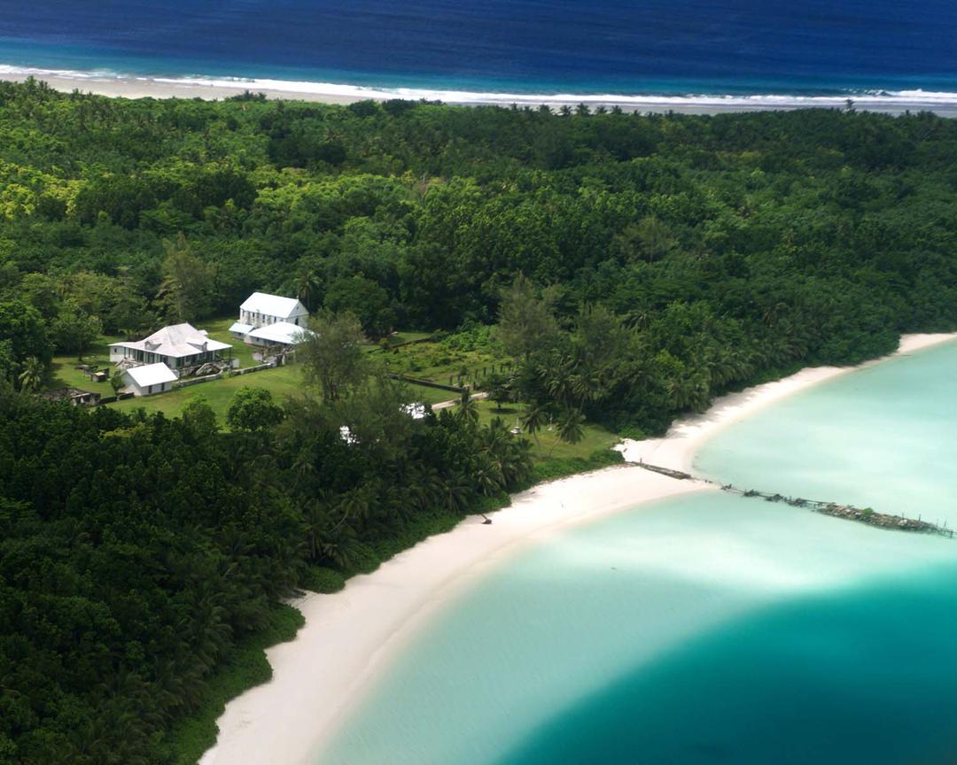 A view of the east point from the air, showing a white house surrounded by trees in the ocean