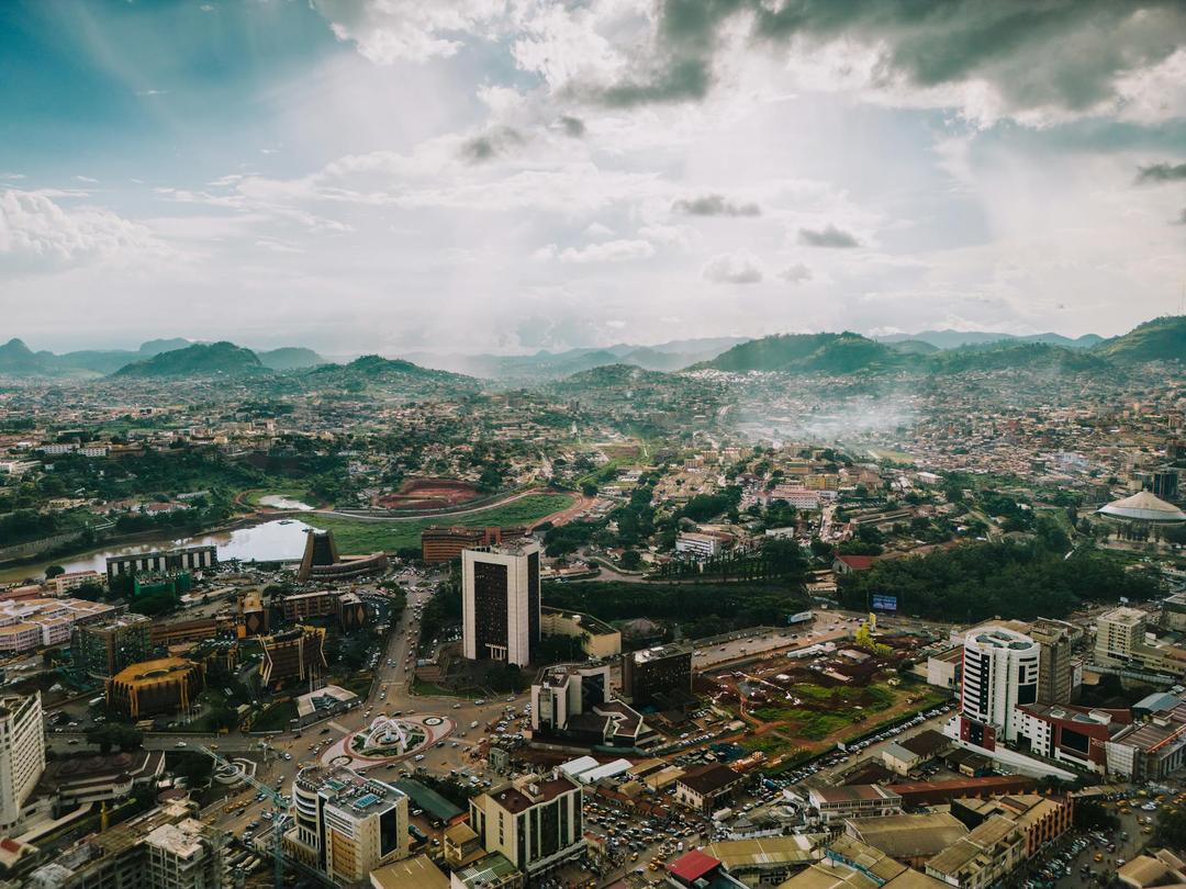 The capital city of Cameroon, Yaounde, depicted by a birds eye view of the city with rolling hills in the background.