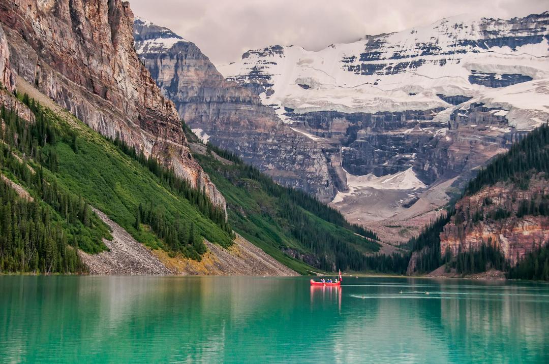 A red boat on a lake surrounded by mountains.