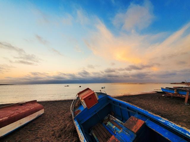 Blue and red boat on beach in front of ocean at sunrise