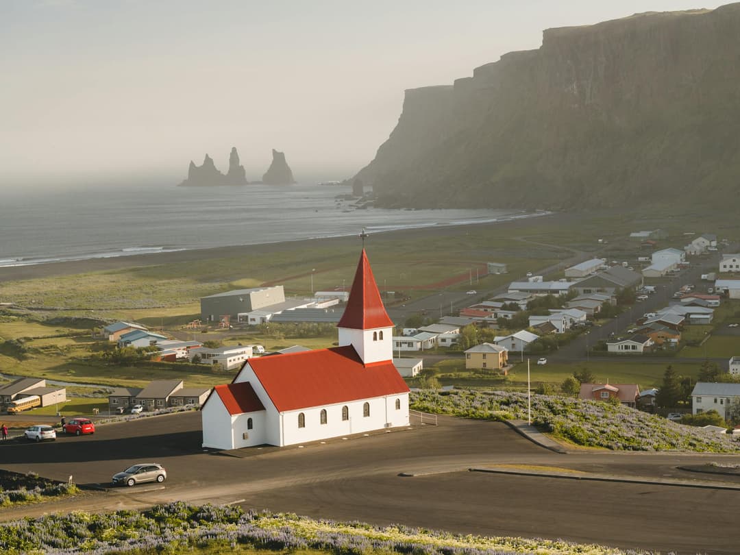 A small village next to the sea, with large cliffs in the background, and a small white building with a red roof