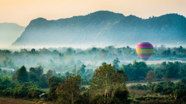 Hot air balloon floating in front of green mountains