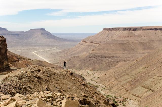 Person standing at the edge of a rock mountain facing the mountains