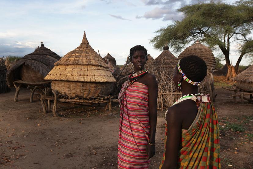 Two people in south sudan standing in front of round wooden huts